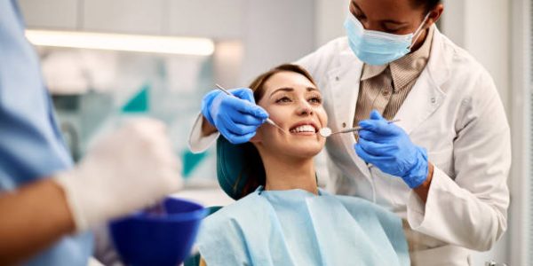 ortodontia Smiling woman getting her teeth checked by African American dentist at dental clinic.